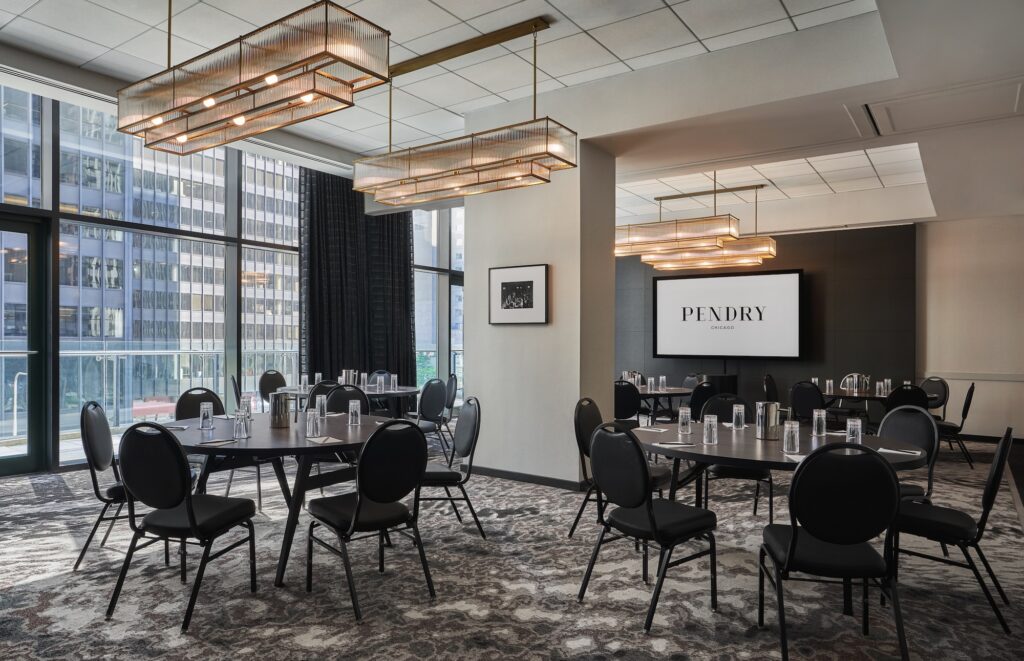 Meeting room with round tables, black chairs, large windows, and a screen