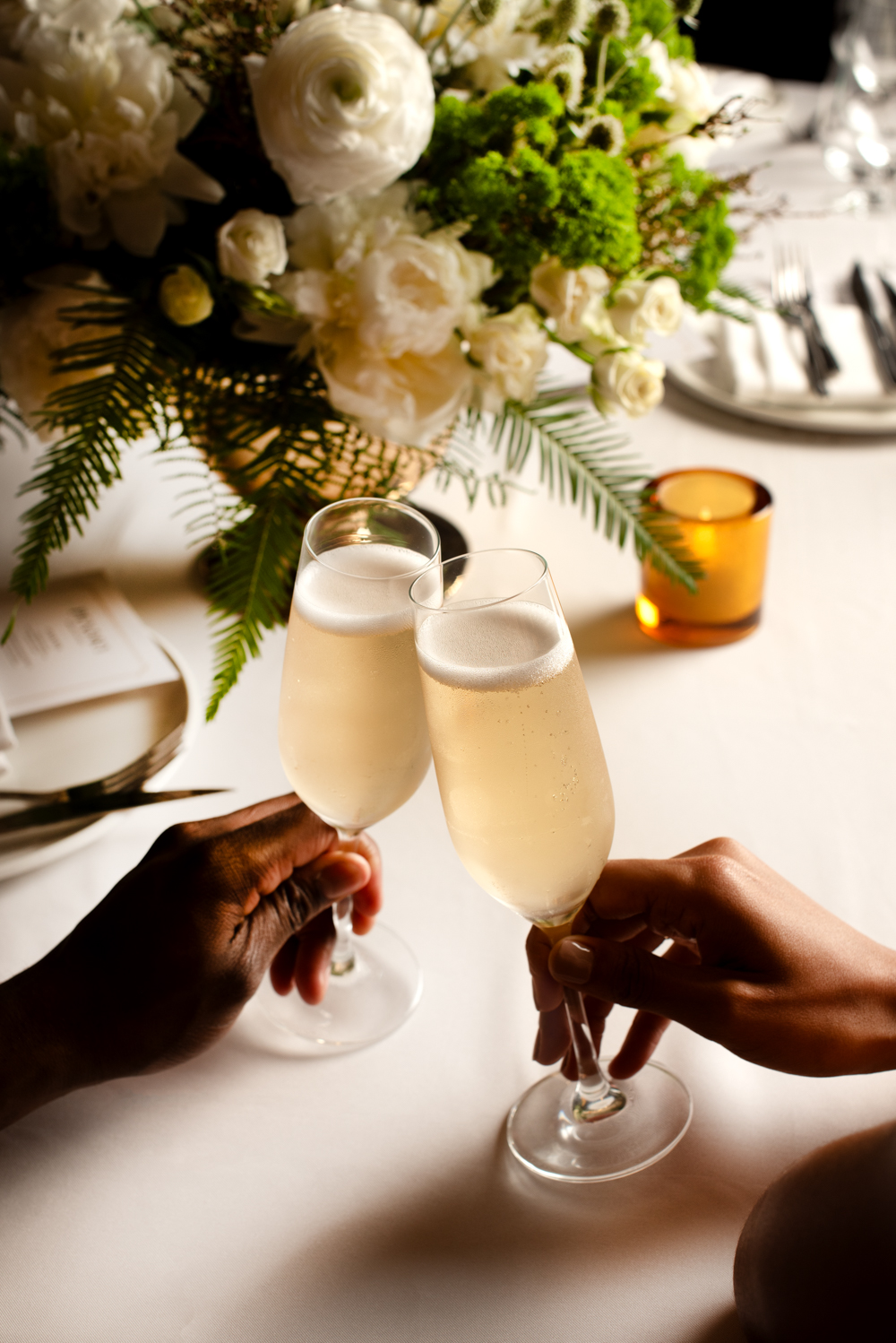 Two people clinking champagne glasses at a table with flowers and candles