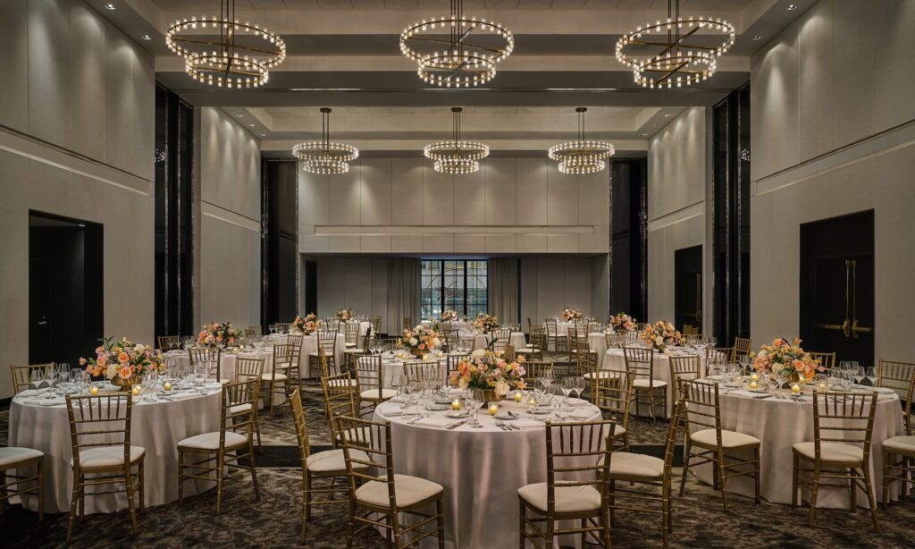 Ballroom with round tables, floral centerpieces, gold chairs, and modern chandeliers