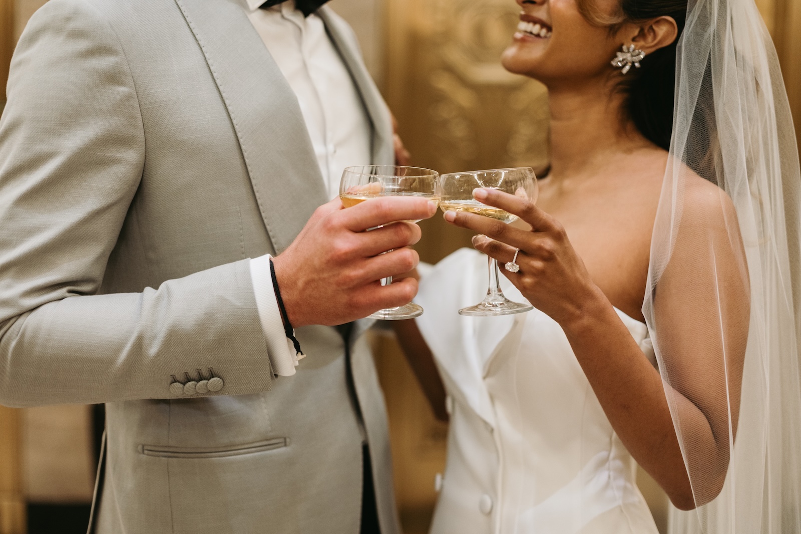 A bride and groom toast with coupe glasses of champagne, smiling warmly