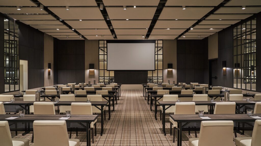 Conference room with rows of tables and chairs facing a large projection screen.