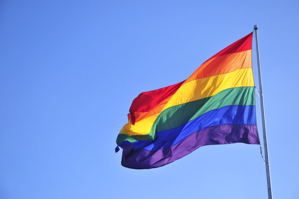 Rainbow flag over blue sky.