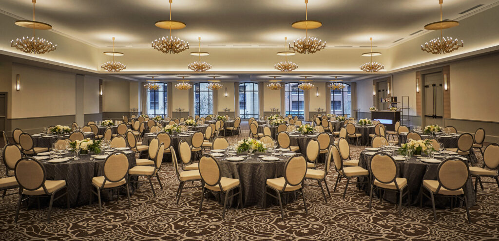 Ballroom set with round tables, floral centerpieces, and modern chandeliers