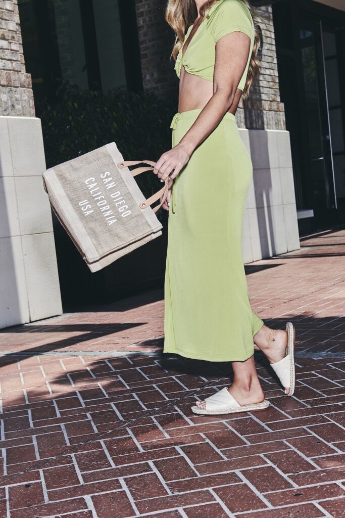 Woman in a green outfit carrying a tote bag that reads “San Diego California USA”