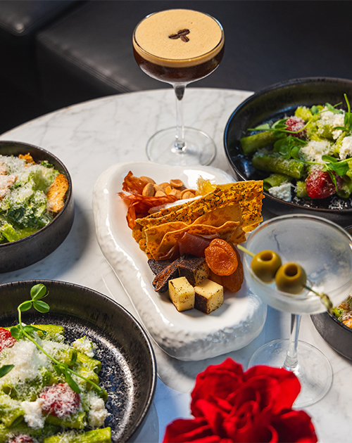 Four plates of salad next to two cocktails and a charcuterie board
