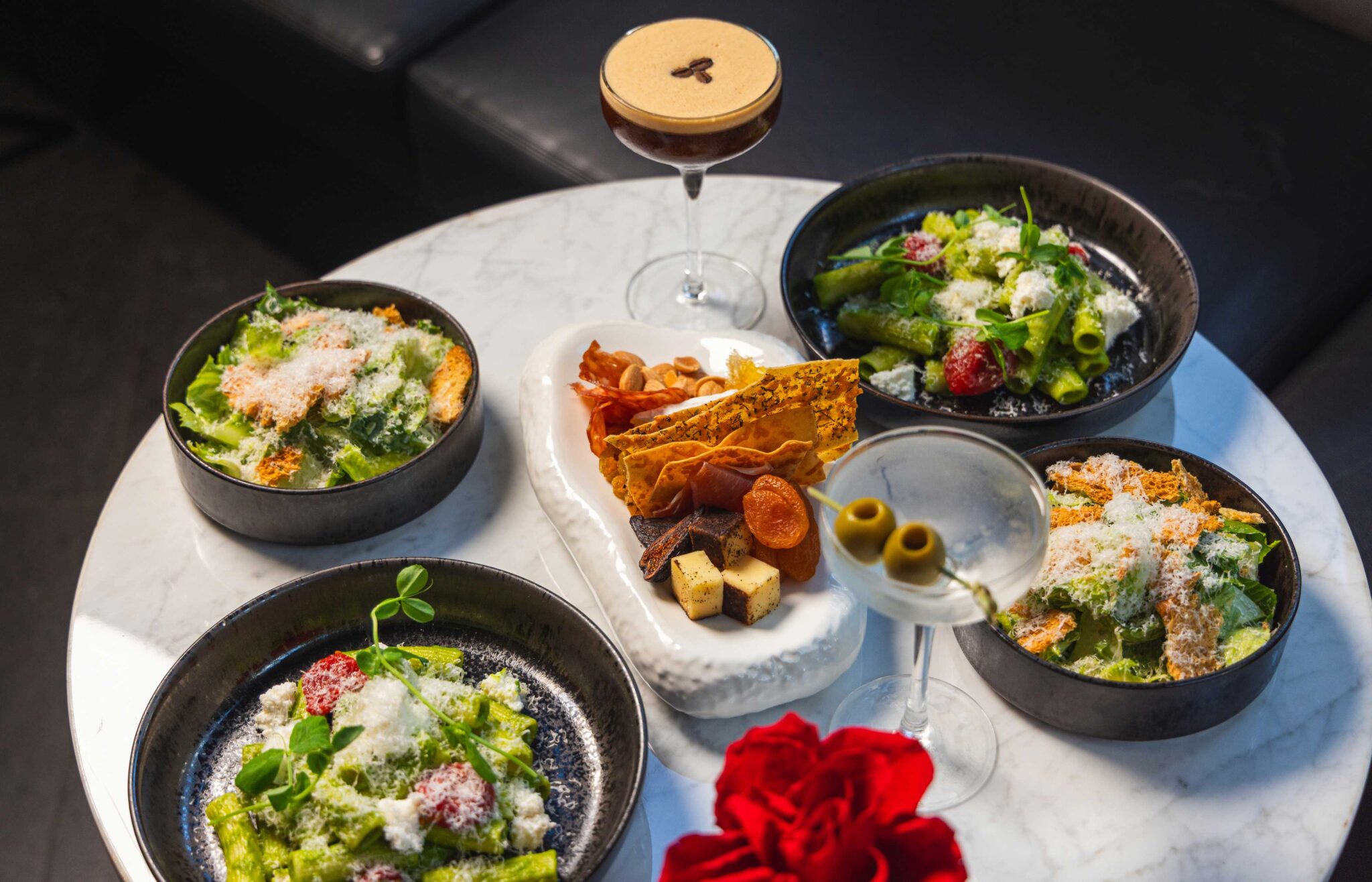Four plates of salad next to two cocktails and a charcuterie board