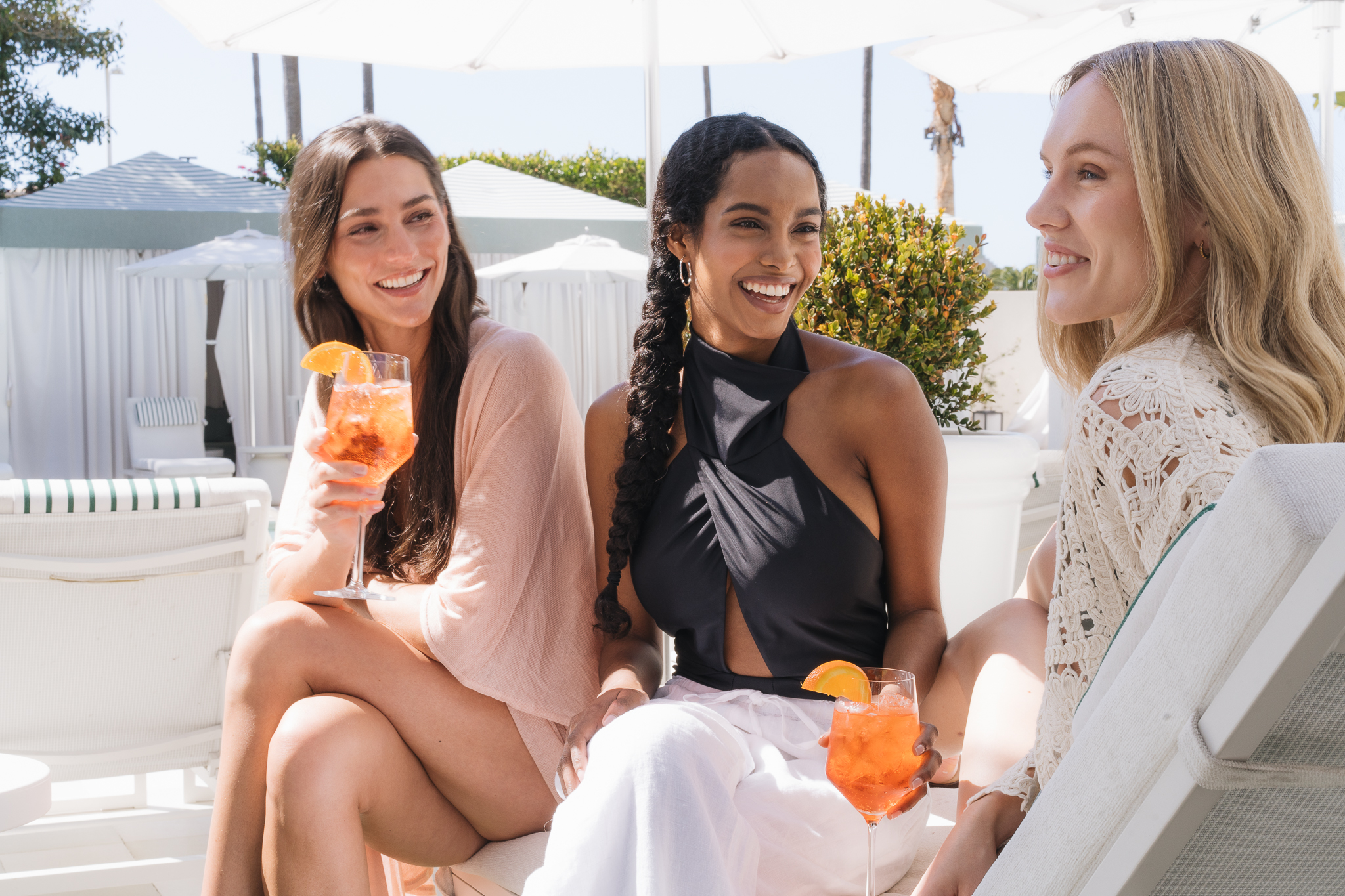 3 women hanging by the pool drinking a cocktail.