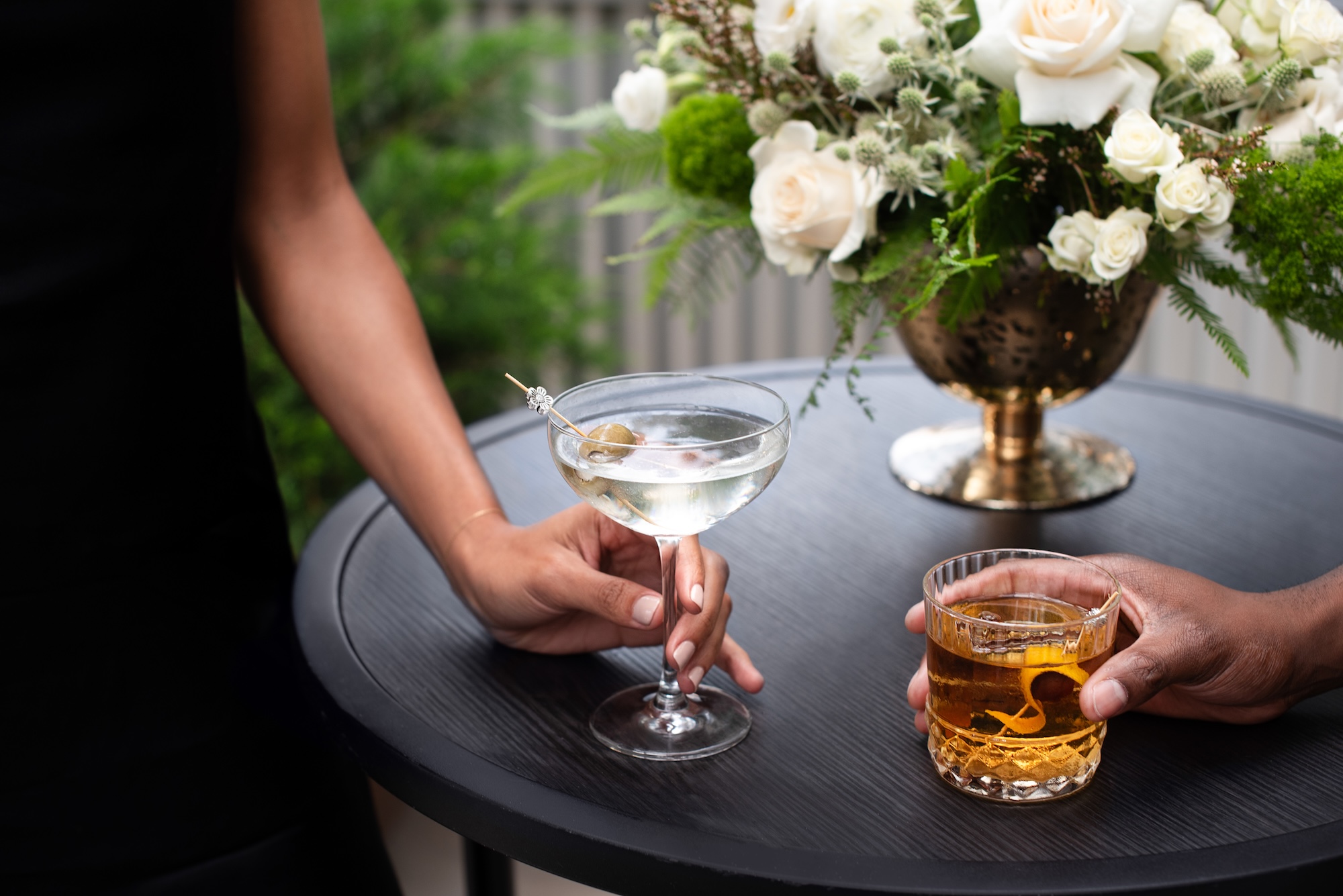 Two people holding cocktails at a table with a floral centerpiece