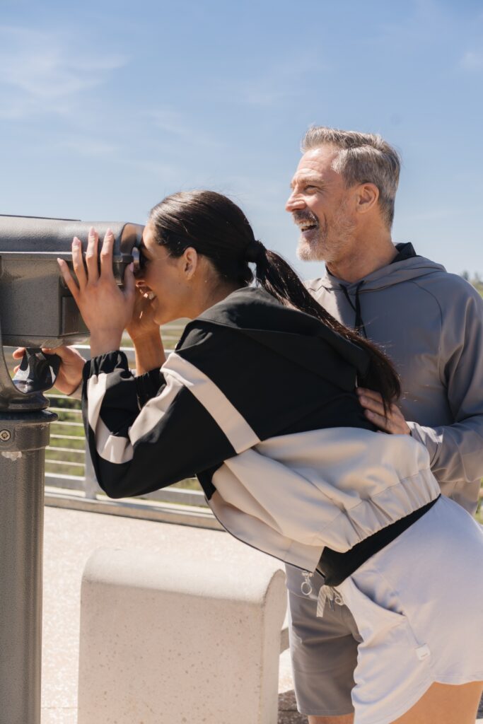 Smiling couple using a public binocular viewer outdoors on a sunny day