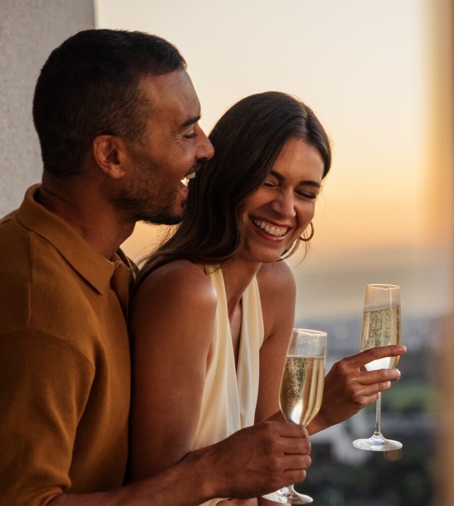 Couple laughing with champagne on a balcony at sunset
