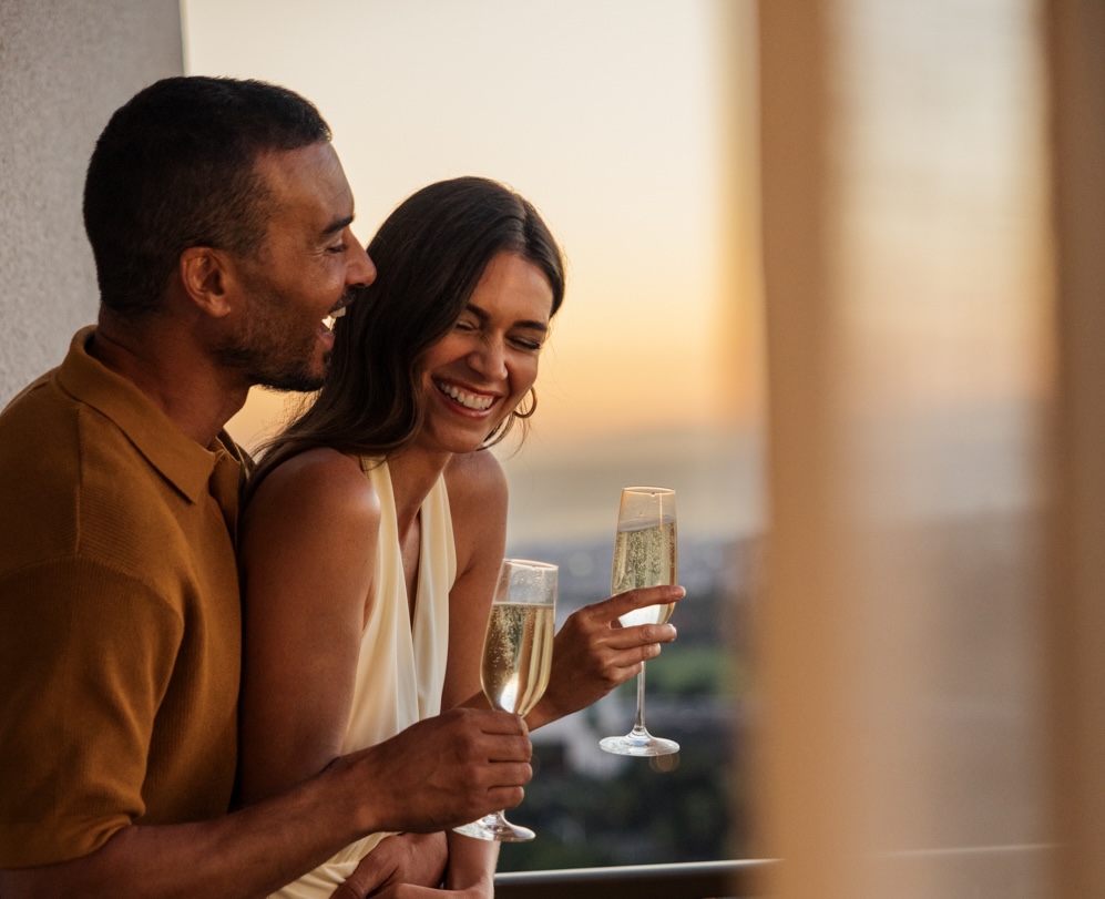 Couple laughing with champagne on a balcony at sunset
