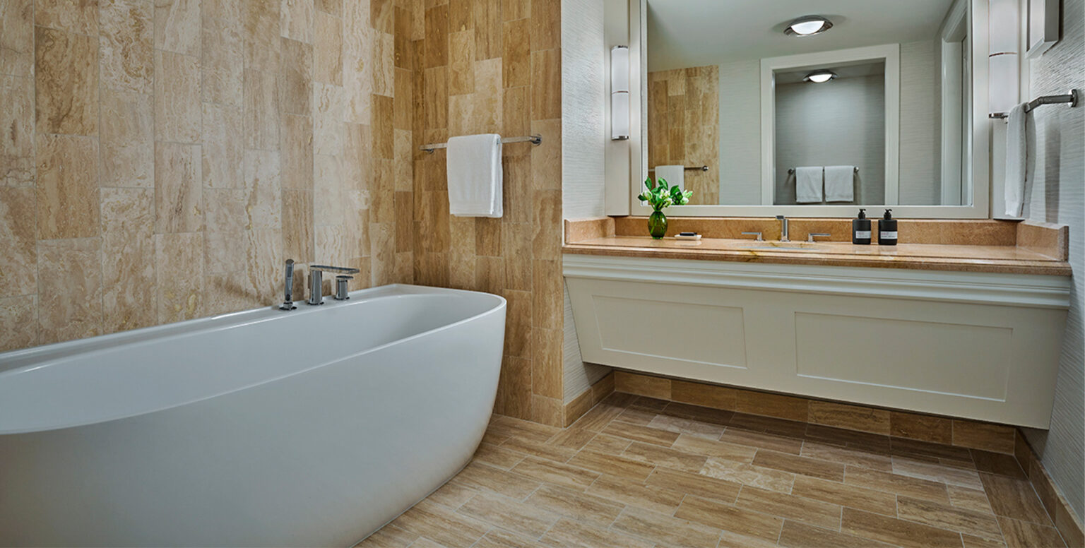 A white bathtub and marble vanity in a guestroom at Pendry Newport Beach