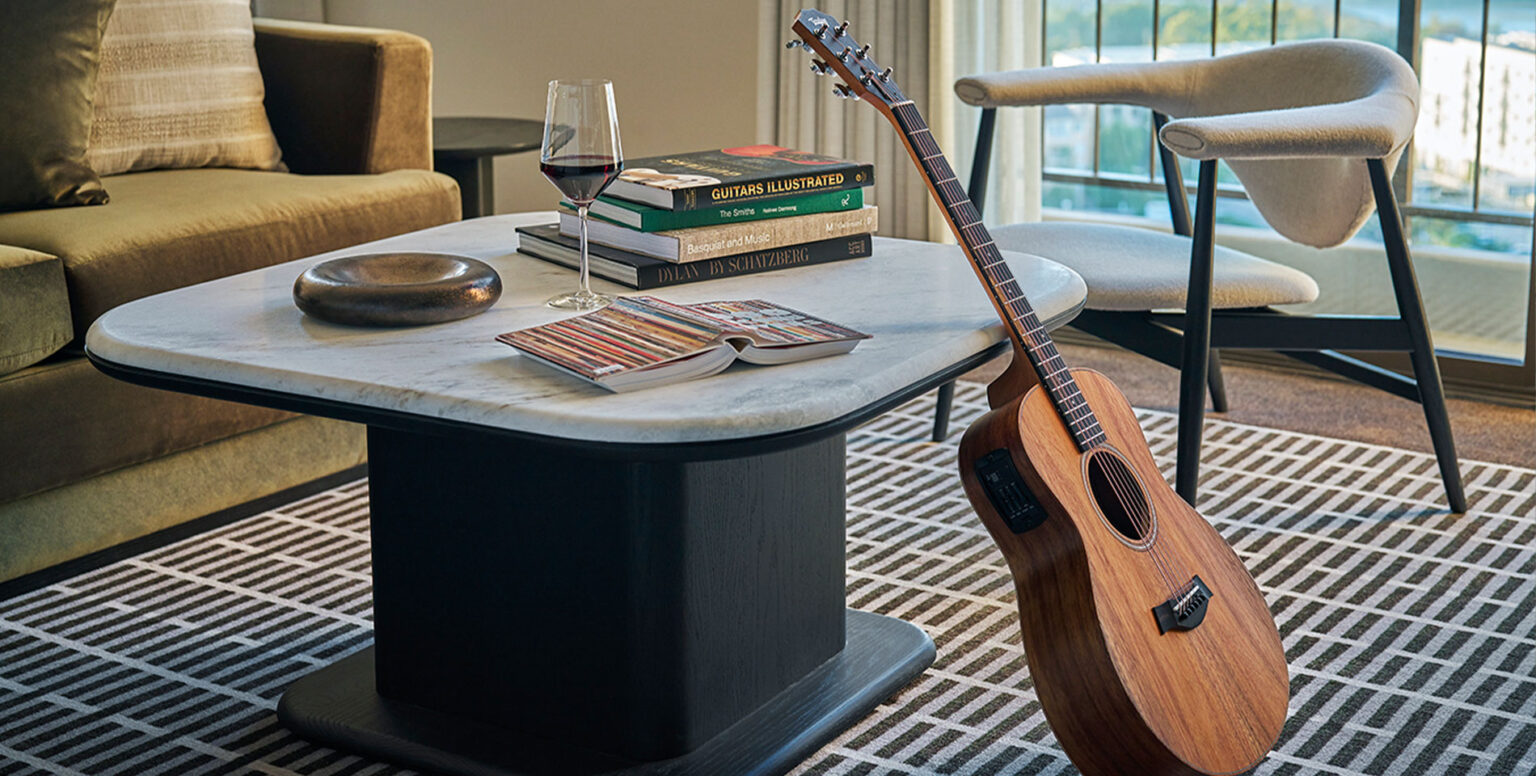 A guitar leaning on a coffee table with a glass of wine on it at Pendry Newport Beach