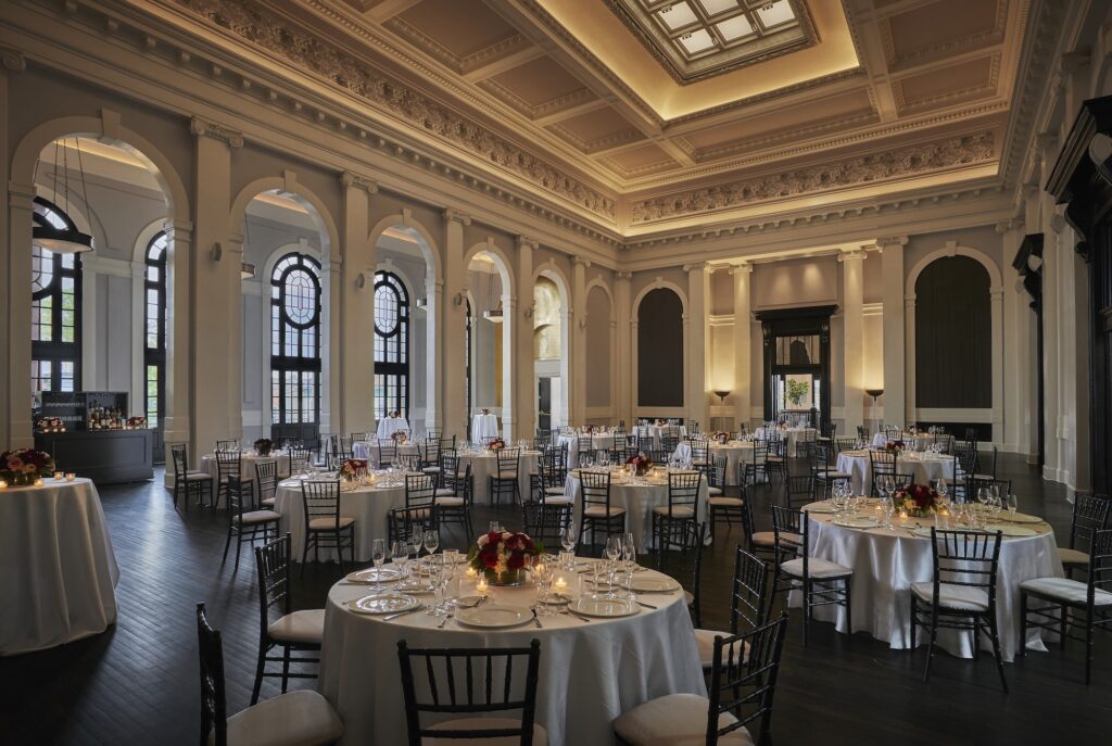 Grand ballroom with high ceilings, arched windows, round tables, and elegant dinner settings