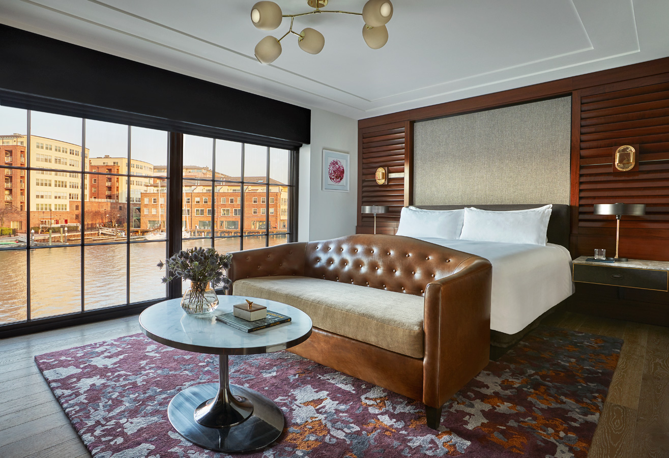 Hotel room with a large bed, leather sofa, and riverfront view through floor-to-ceiling windows