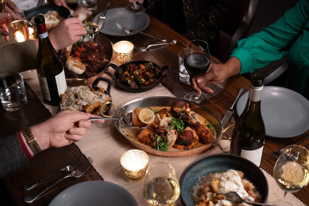 Dinner table with shared dishes, wine, and people enjoying a meal together