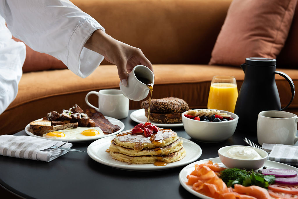 In-room breakfast at Pendry Manhattan West with pancakes topped with strawberries, eggs, bacon, toast, fruit and orange juice.