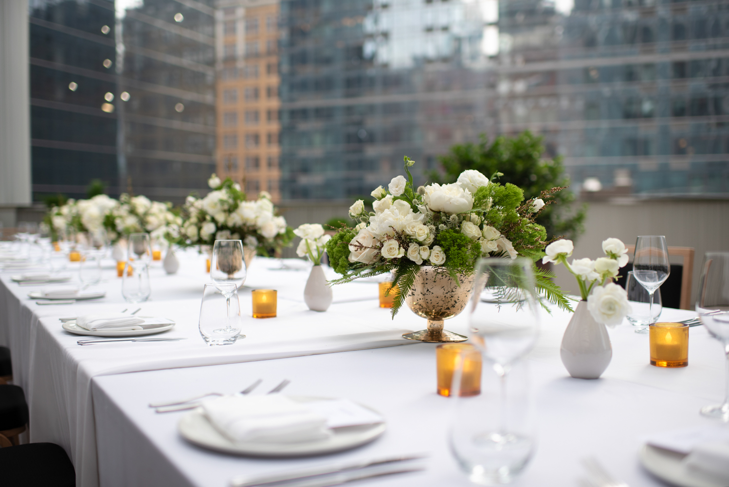 Elegant outdoor event setup at The Salon & Terrace with white floral centerpieces, candles, and city skyline views at Pendry Manhattan West.