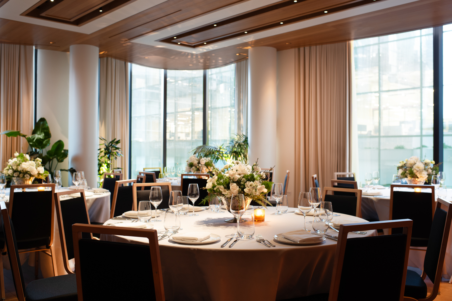 Wedding reception setup with round tables, floral centerpieces, candles and floor-to-ceiling windows at Pendry Manhattan West.