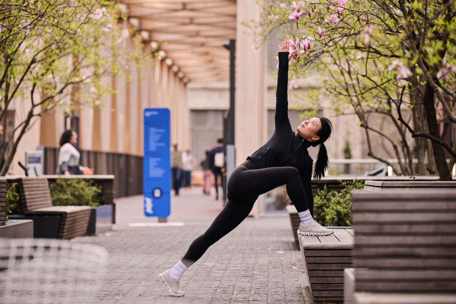 Person stretching outdoors among trees and benches near Pendry Manhattan West.