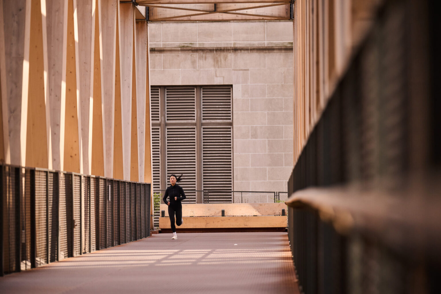 A Person jogging on a bridge near Pendry Manhattan West surrounded by modern architectural structures.