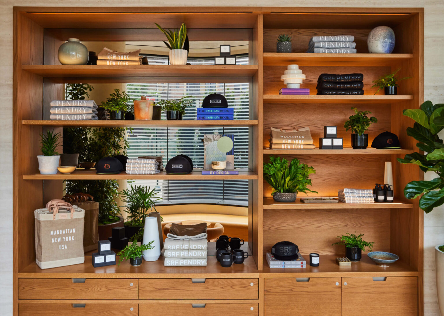 Retail display at Pendry Manhattan West featuring branded apparel, hats and candles on wooden shelves.