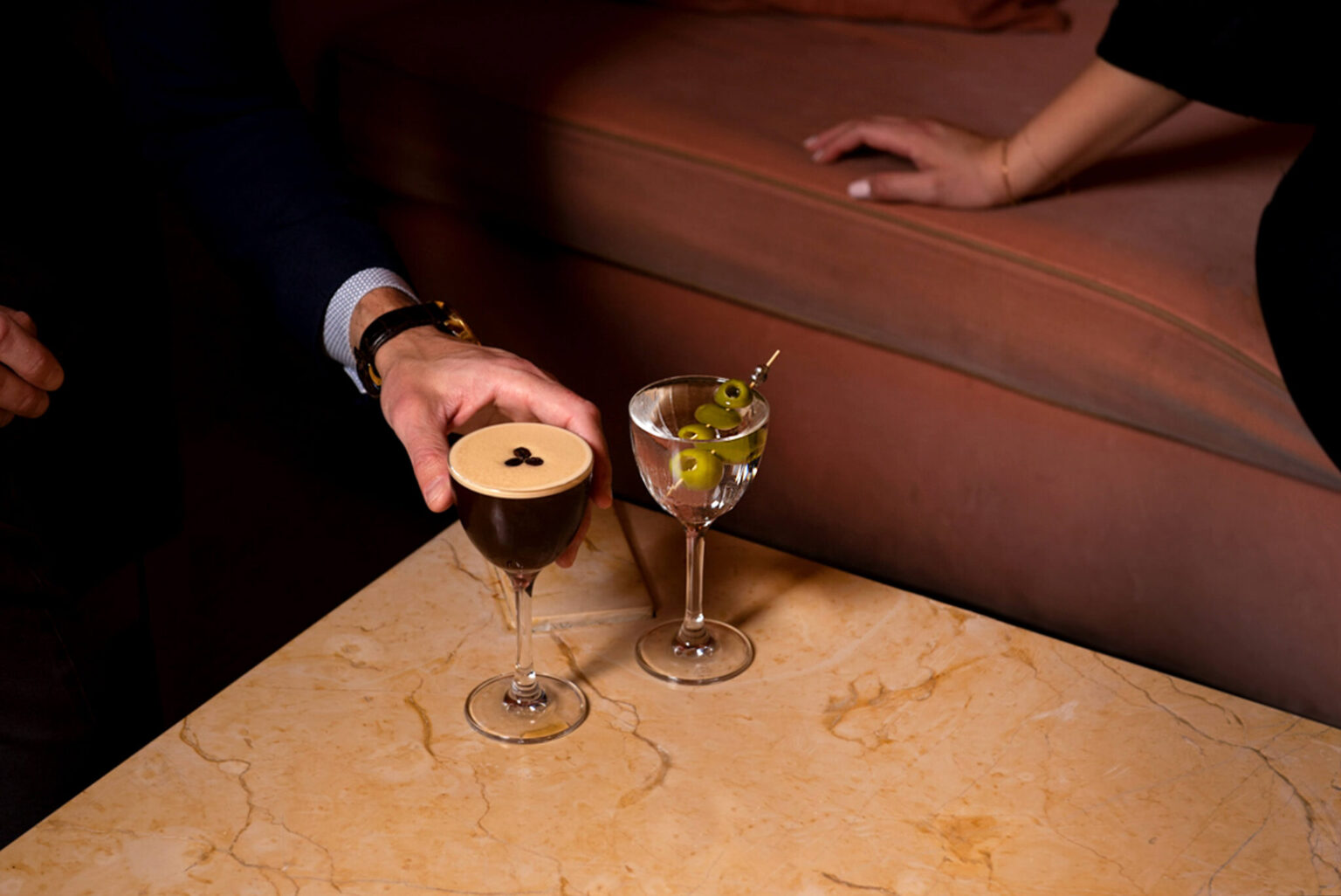 An espresso martini and a martini with olives, on a marble table at Pendry Manhattan West.