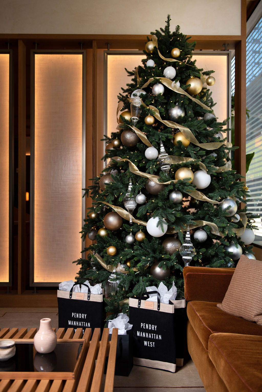A Christmas tree decorated in gold, bronze, and silver ornaments with ribbon garland stands in a modern lounge