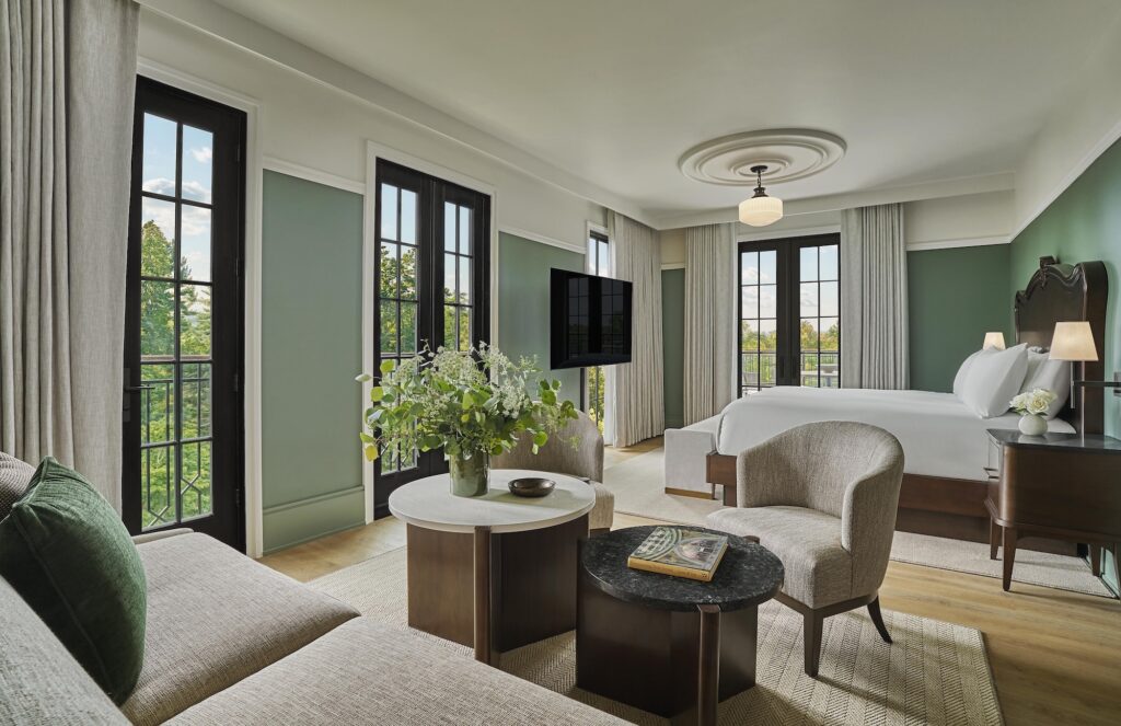 Hotel room with a large bed, sitting area, and French doors opening to garden views