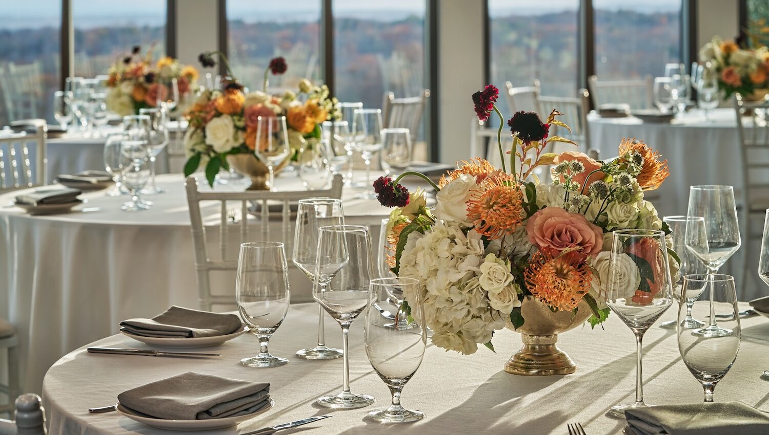 Elegant ballroom setup with round tables draped in white linens, set with glassware and silverware, and decorated with vibrant floral centerpieces featuring roses