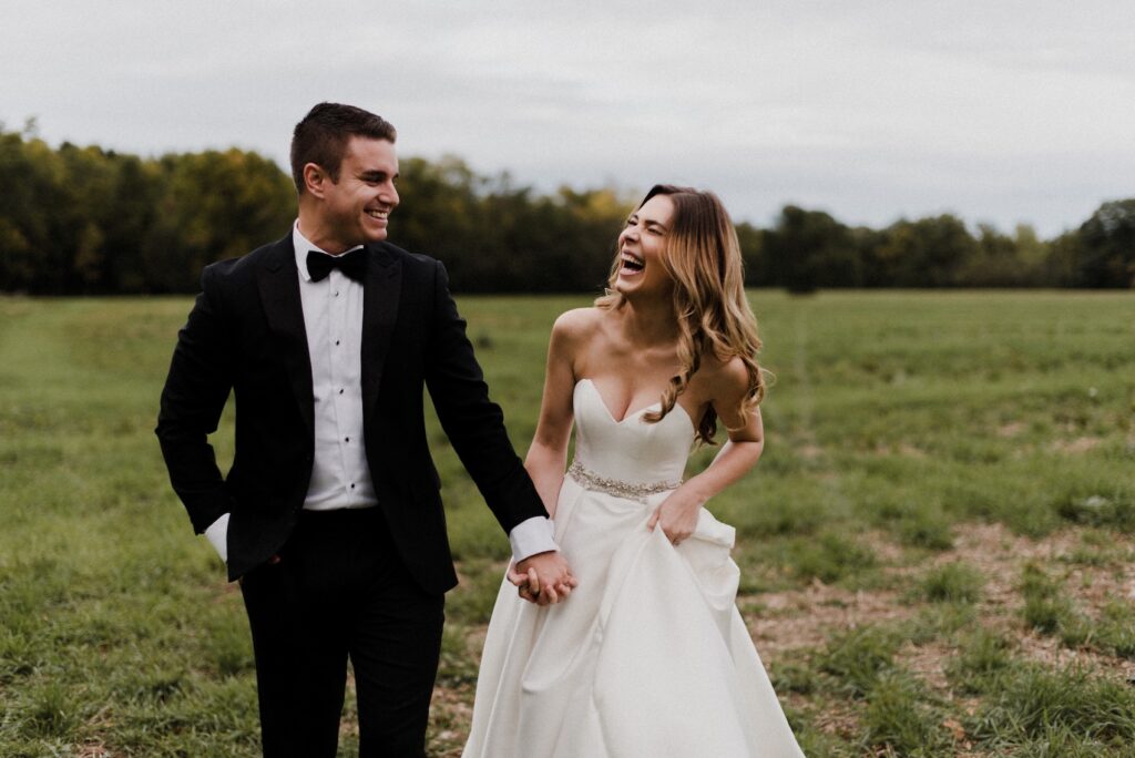 Bride and groom walk hand in hand through a grassy field