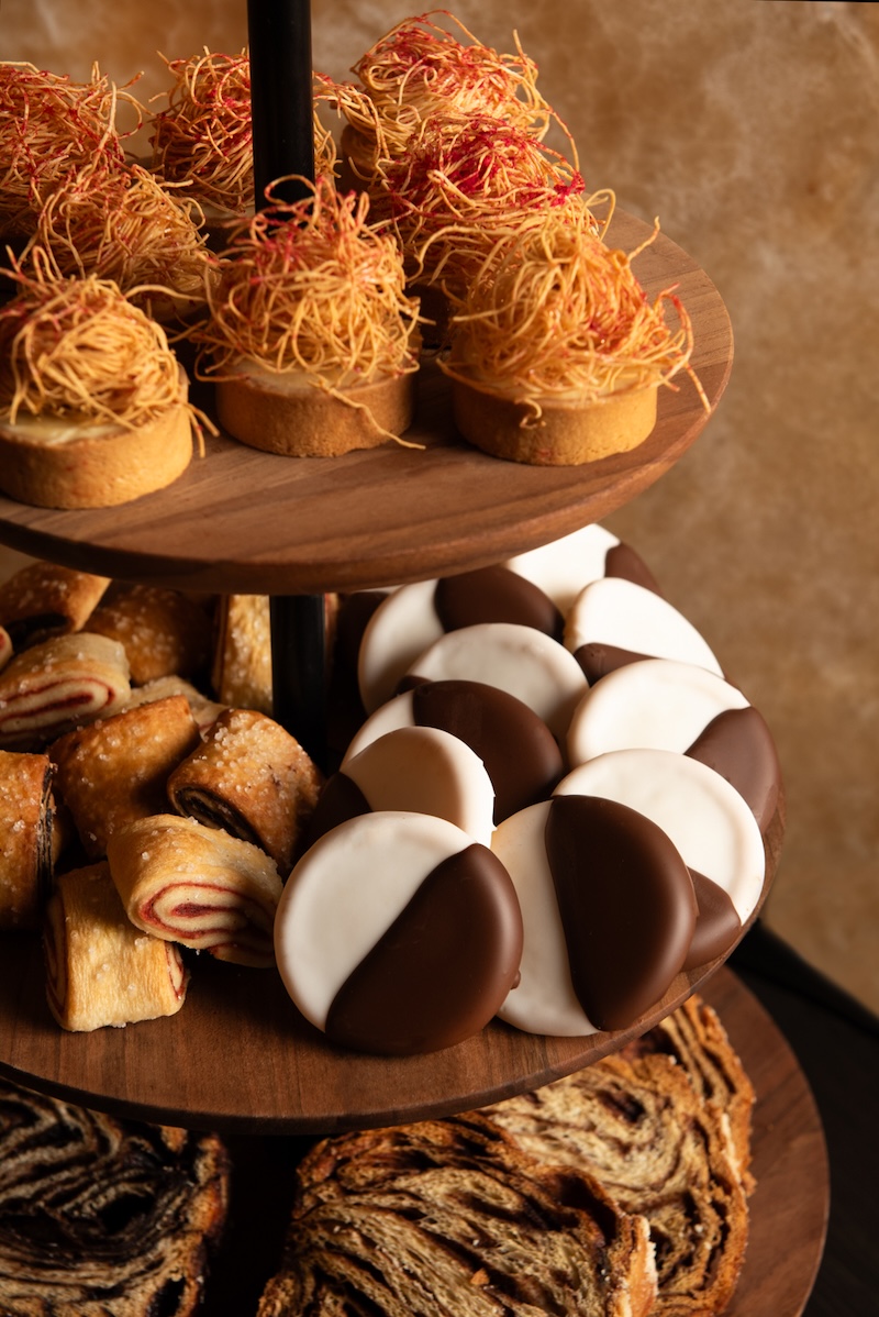 A tiered wooden dessert stand filled with a variety of pastries and sweets