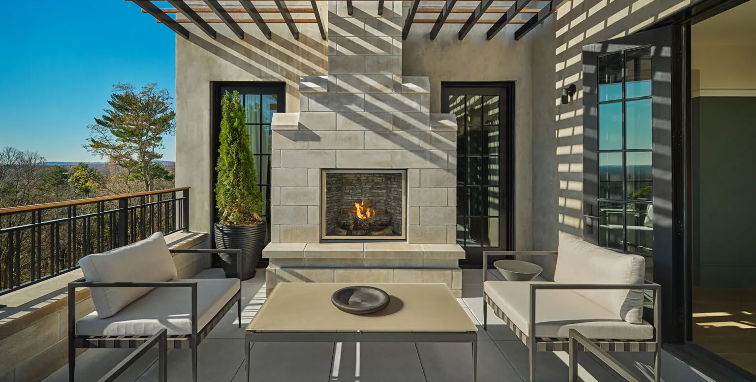 An outdoor patio with a stone fireplace, two sofas and coffee table outside of a suite at Pendry Natirar