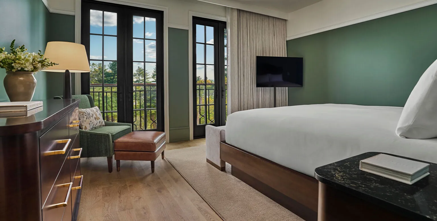 A queen bed in a guestroom facing floor to ceiling french doors overlooking the New York countryside at Pendry Natirar
