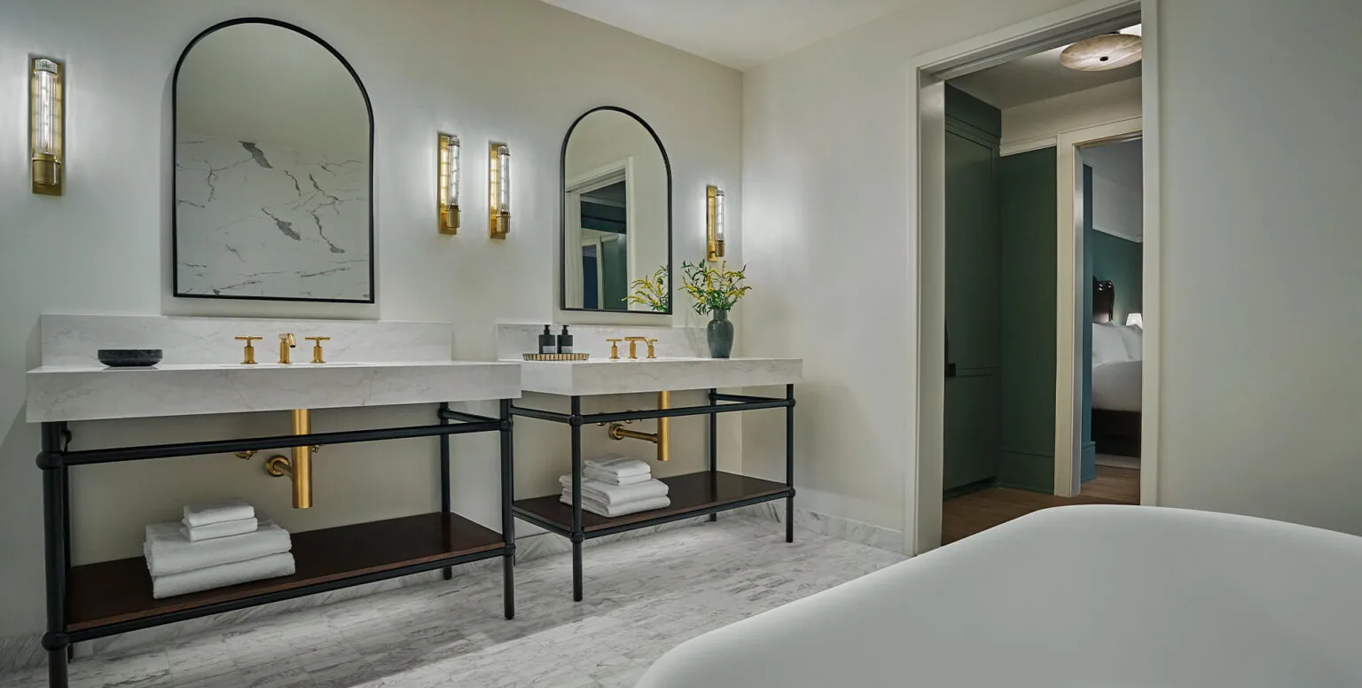 Two vanities in a white bathroom with a tub in the corner at Pendry Natirar resort