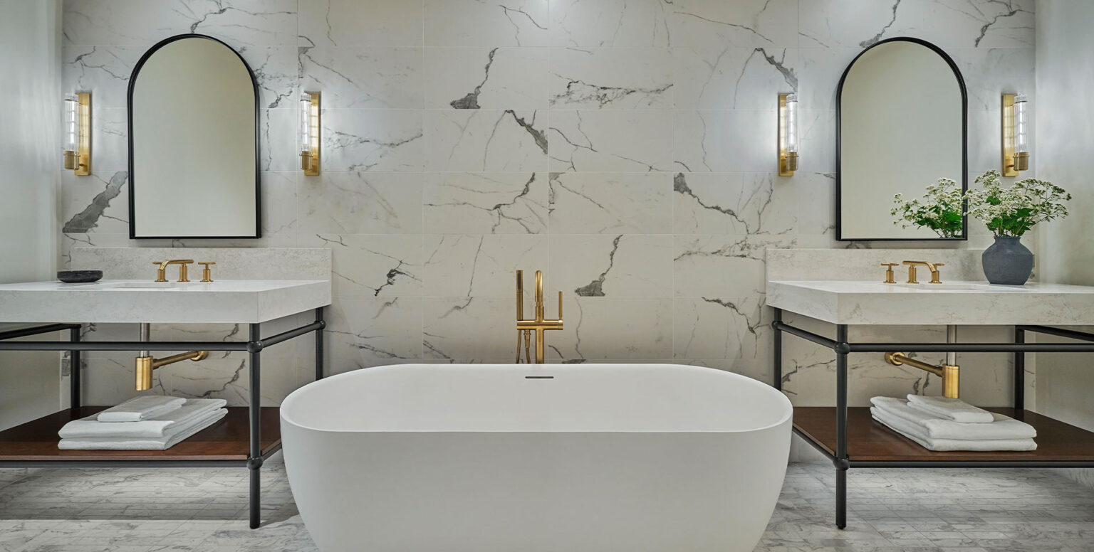 A suite bathroom at Pendry Natirar with marble walls, two vanities and a bathtub
