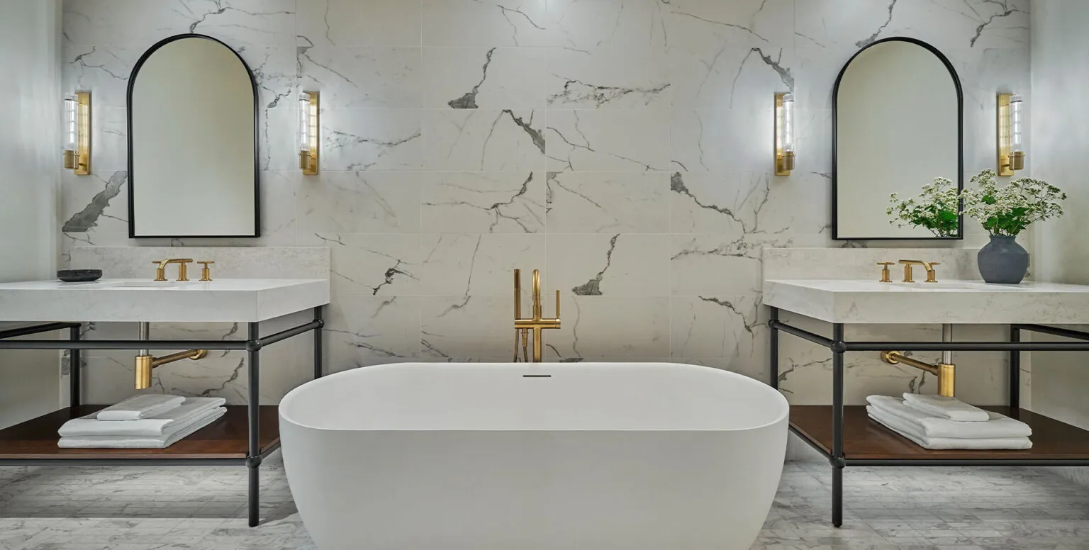 A suite bathroom at Pendry Natirar with marble walls, two vanities and a bathtub