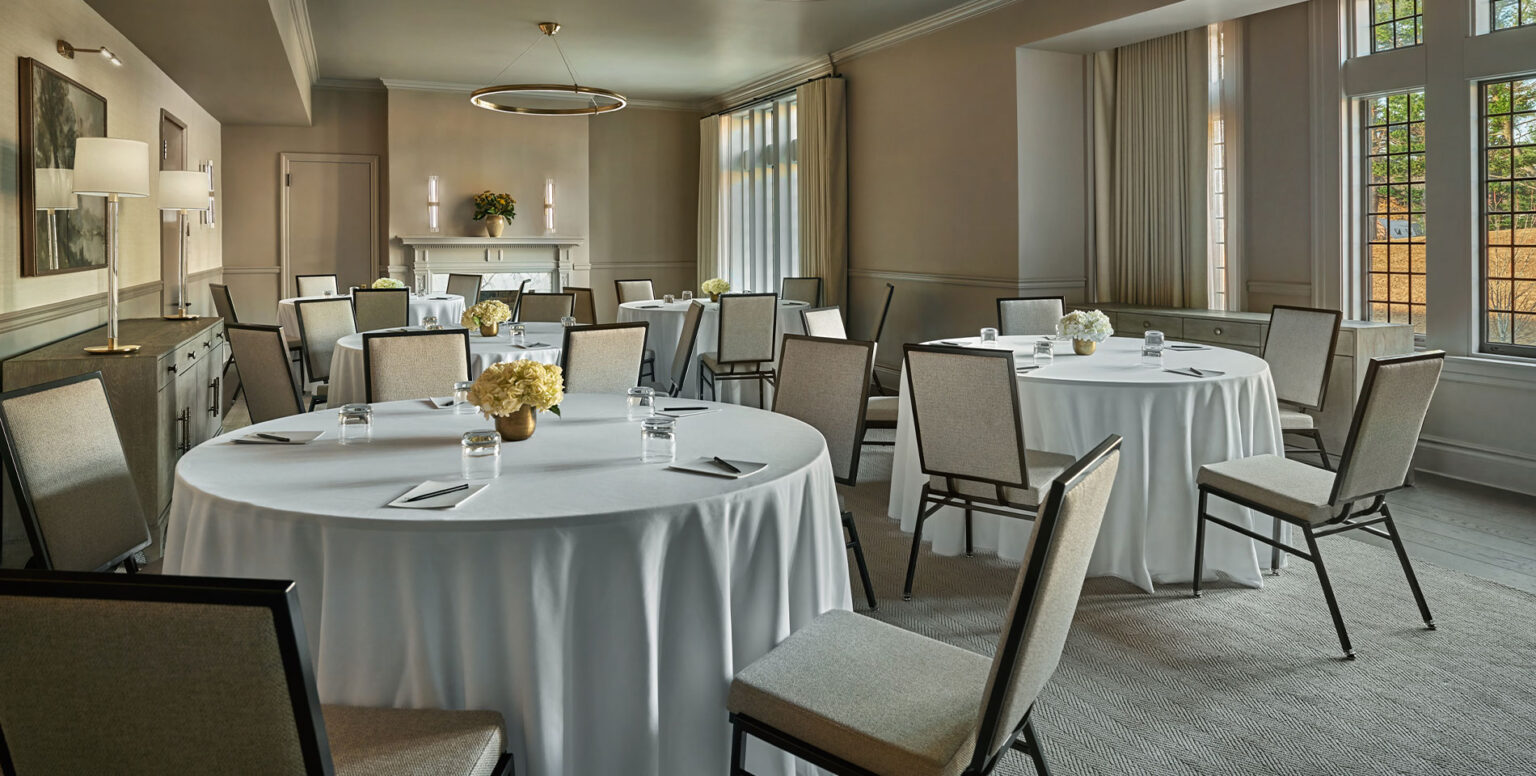A meeting space with white table clothed tables with chairs around the tables at Pendry Natirar