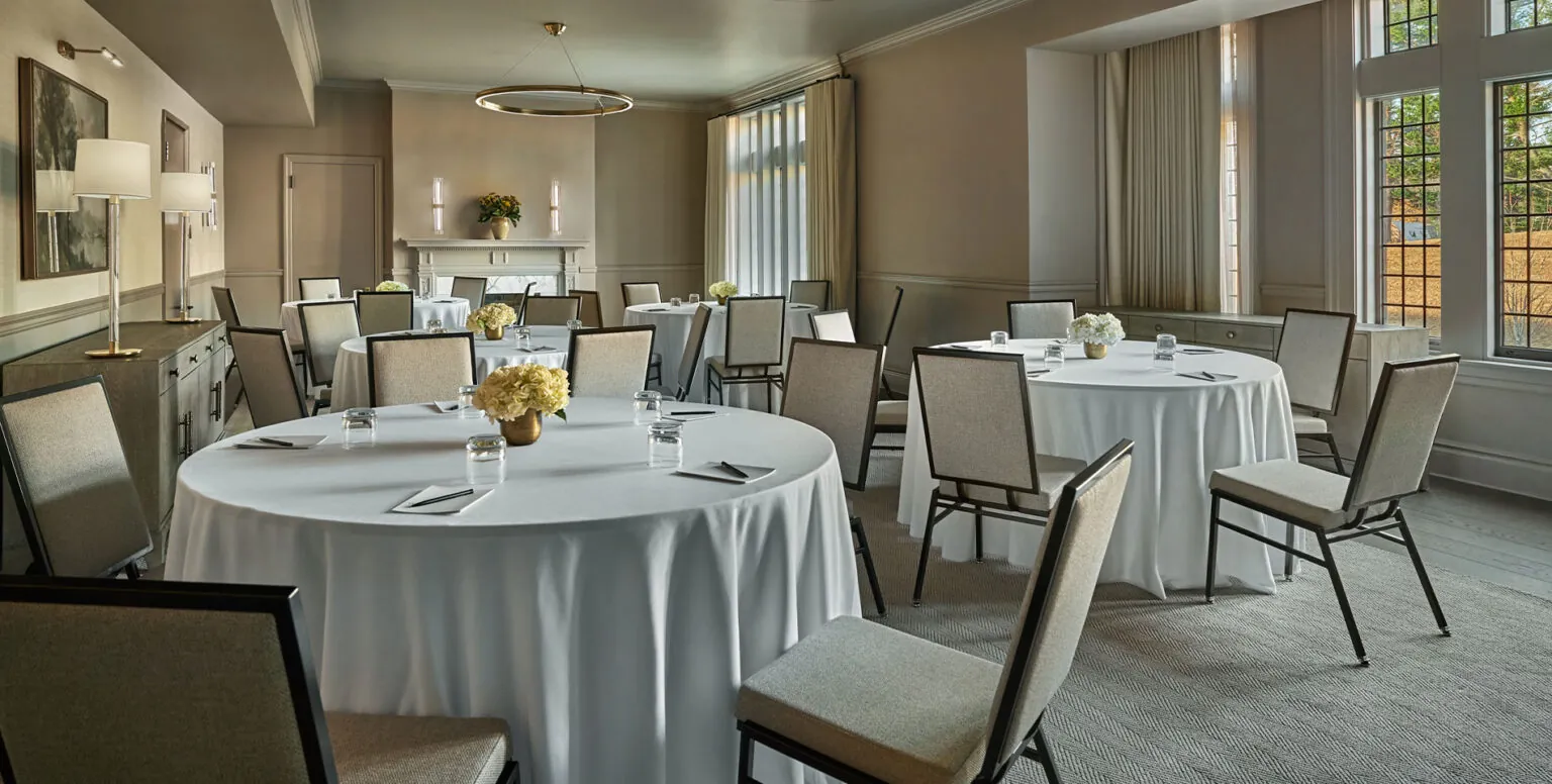 A meeting space with white table clothed tables with chairs around the tables at Pendry Natirar