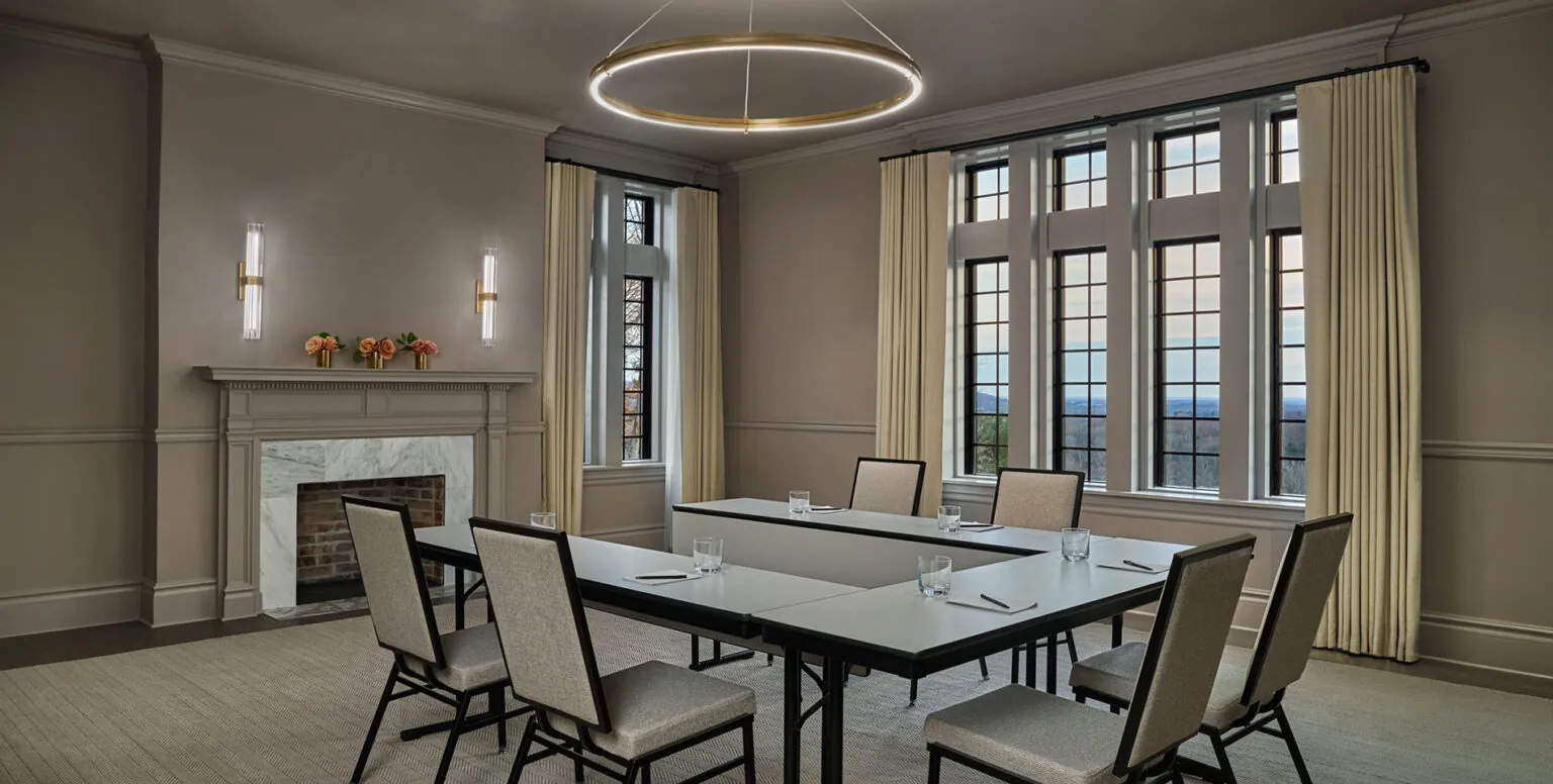 A U-shaped table with white chairs around it in a conference room at Pendry Natirar
