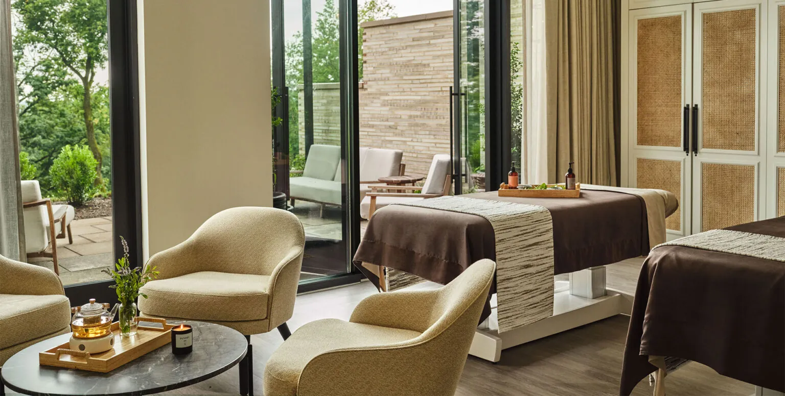 A massage room with two massage tables, three chairs and an outdoor patio at Spa Pendry Natirar