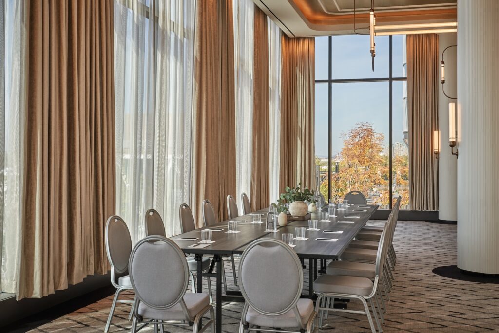 Conference room with a long table, gray chairs, large windows, and floor-to-ceiling curtains.