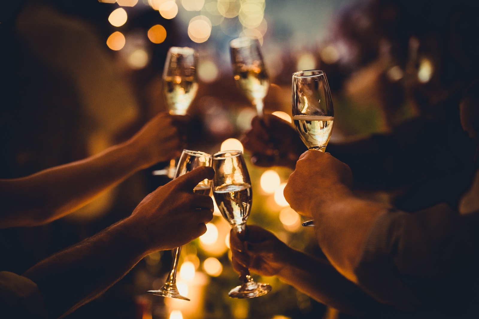 Hands clinking champagne glasses together in a celebratory toast with warm bokeh lights in the background